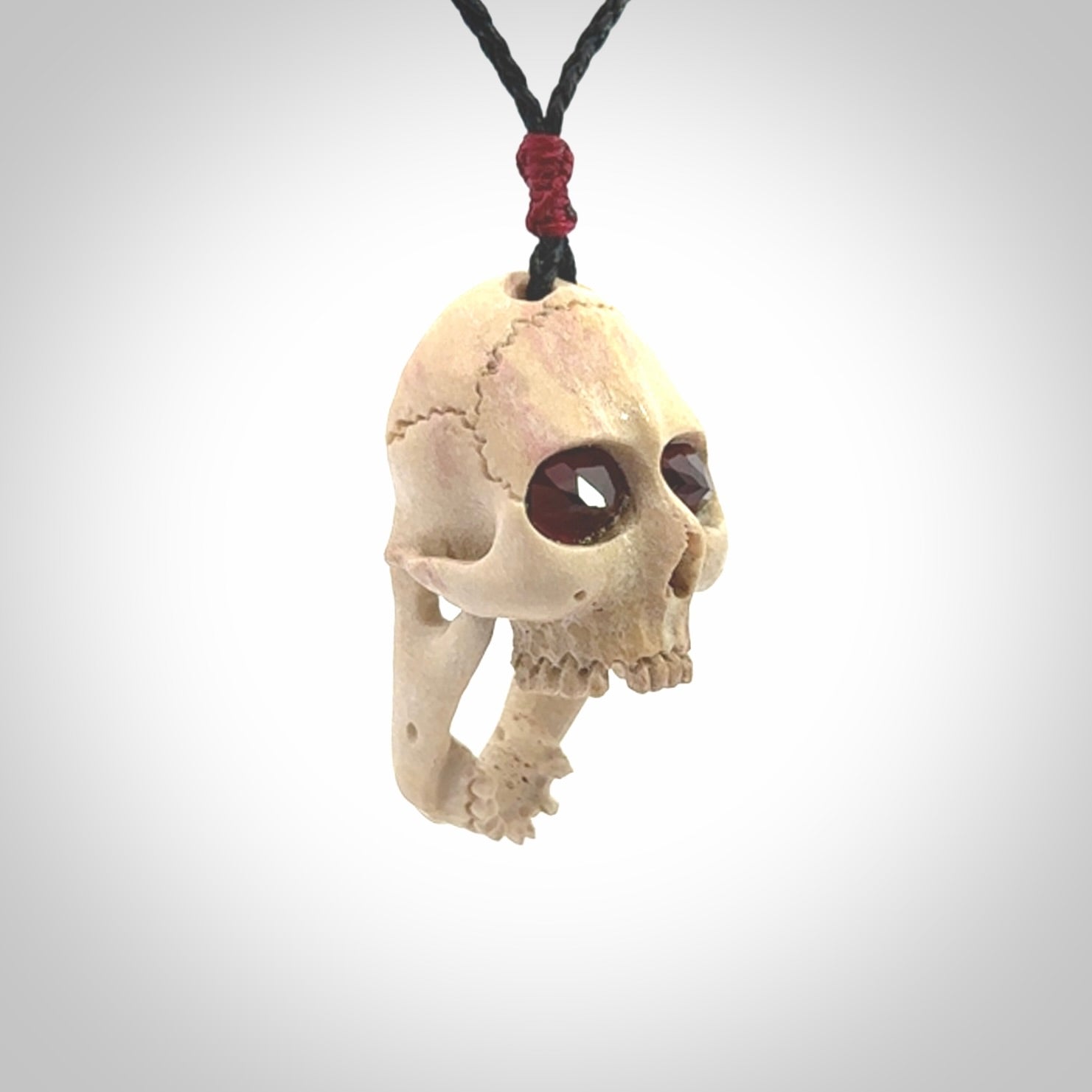 A hand carved SKULL pendant made from deer antler with Pyrope Garnet eyes. This is a work of art carved in deer antler, bone. We deliver this pendant to you on a plaited black cord. Delivery with Express Courier is included in the price.