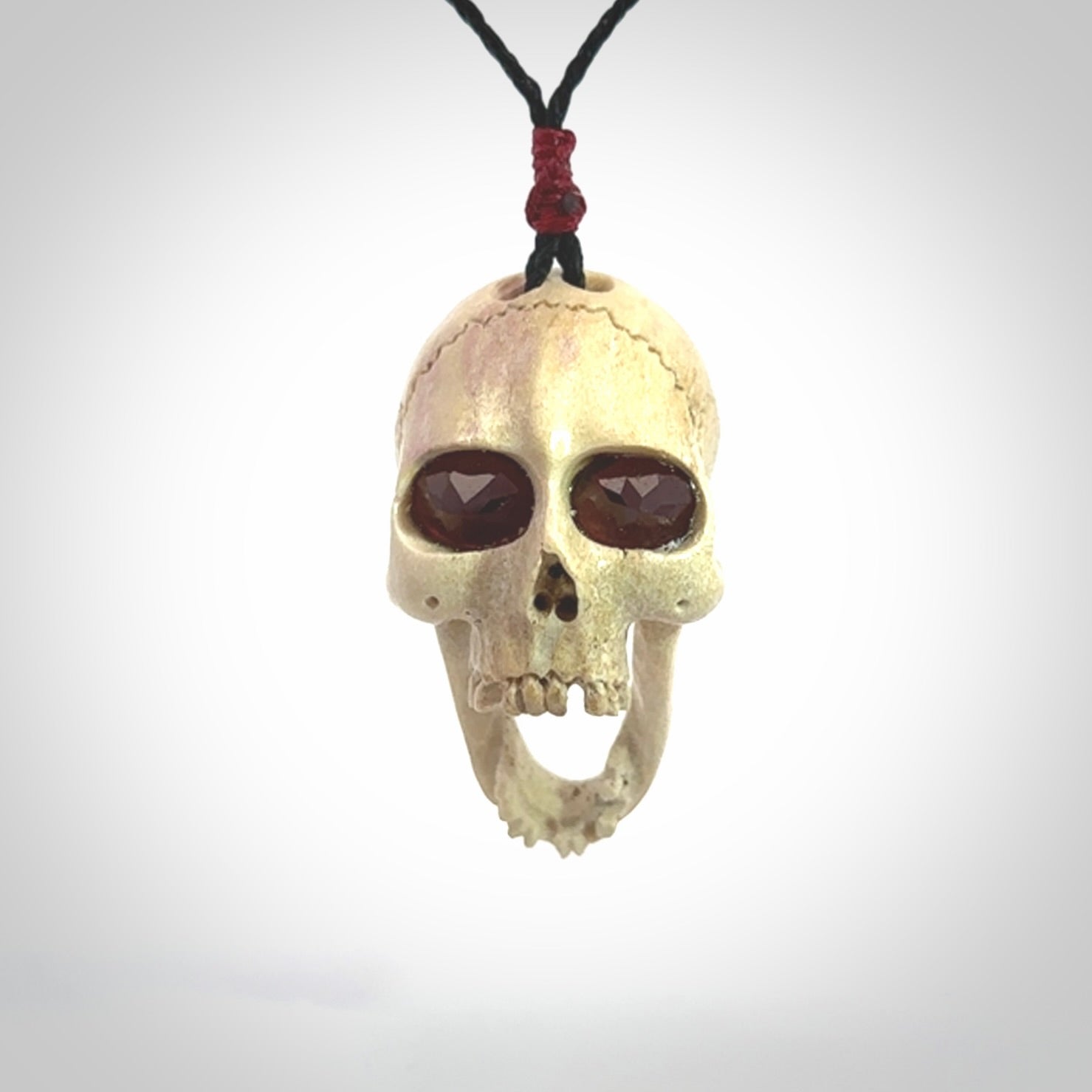 A hand carved SKULL pendant made from deer antler with Pyrope Garnet eyes. This is a work of art carved in deer antler, bone. We deliver this pendant to you on a plaited black cord. Delivery with Express Courier is included in the price.
