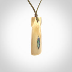 A stunning hand carved Woolly Mammoth Tusk Toki pendant. The toki has a small oval shaped piece of Pāua shell inset into the front face. This piece is bound with an adjustable cord. This is a little piece of Art to wear.