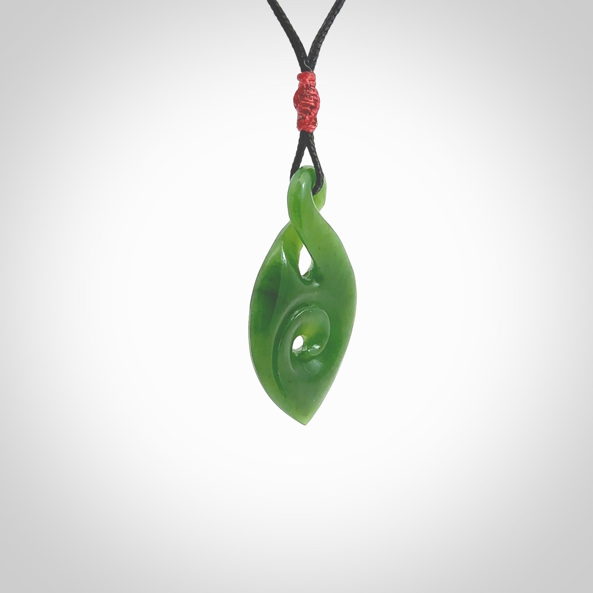 Ross Crump twist with koru pendant. Hand carved from rare New Zealand jade this is a beautiful pounamu pendant. The cord is hand plaited and is length adjustable. It has a little spiral floret popper at the top of the pendant. It is a delicate and very beautiful greenstone pendant. For sale online by NZ Pacific.