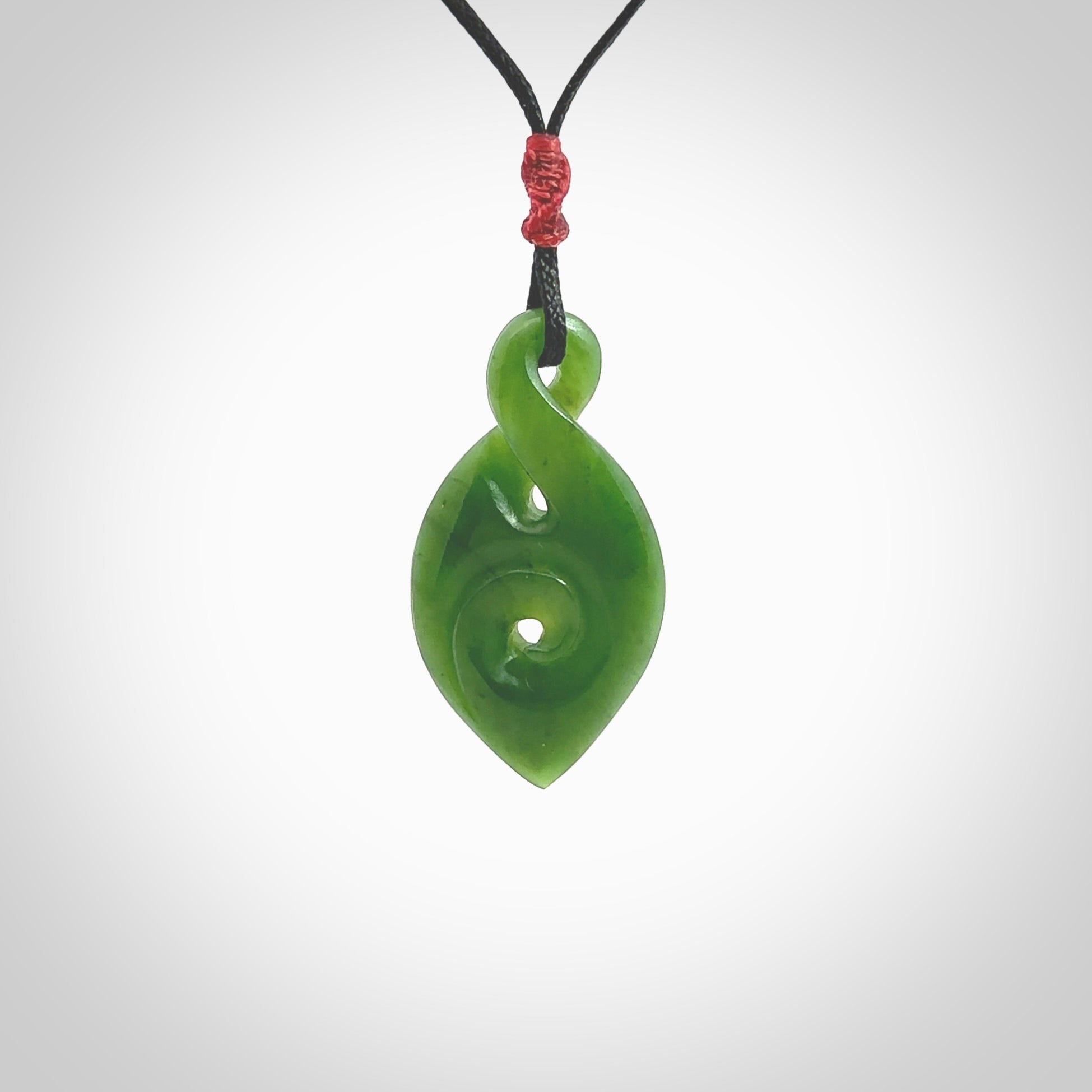 Ross Crump twist with koru pendant. Hand carved from rare New Zealand jade this is a beautiful pounamu pendant. The cord is hand plaited and is length adjustable. It has a little spiral floret popper at the top of the pendant. It is a delicate and very beautiful greenstone pendant. For sale online by NZ Pacific.