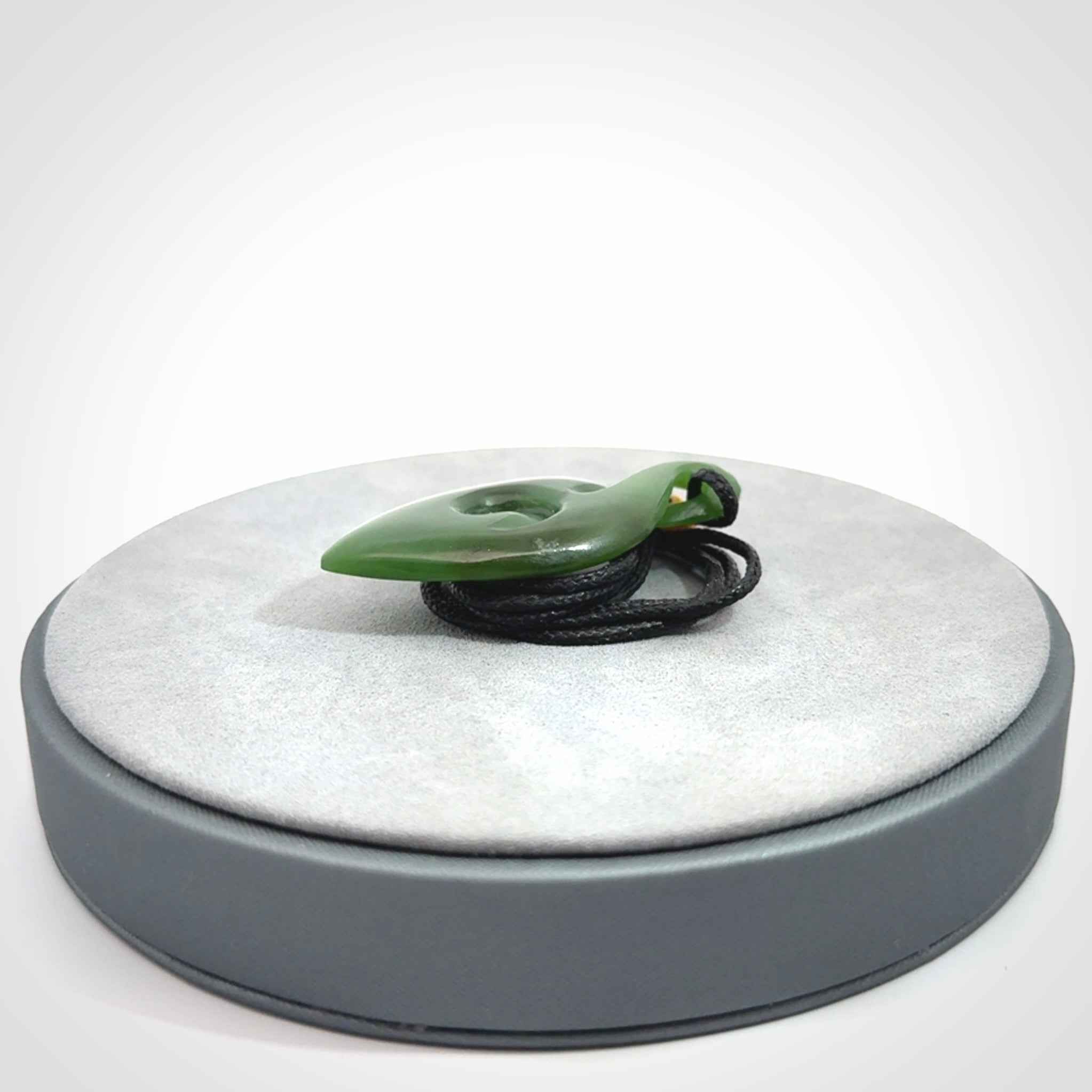 Ross Crump twist with koru pendant. Hand carved from rare New Zealand jade this is a beautiful pounamu pendant. The cord is a black colour and is length adjustable. It has a little spiral floret popper at the top of the pendant. It is a delicate and very beautiful greenstone pendant. For sale online by NZ Pacific.