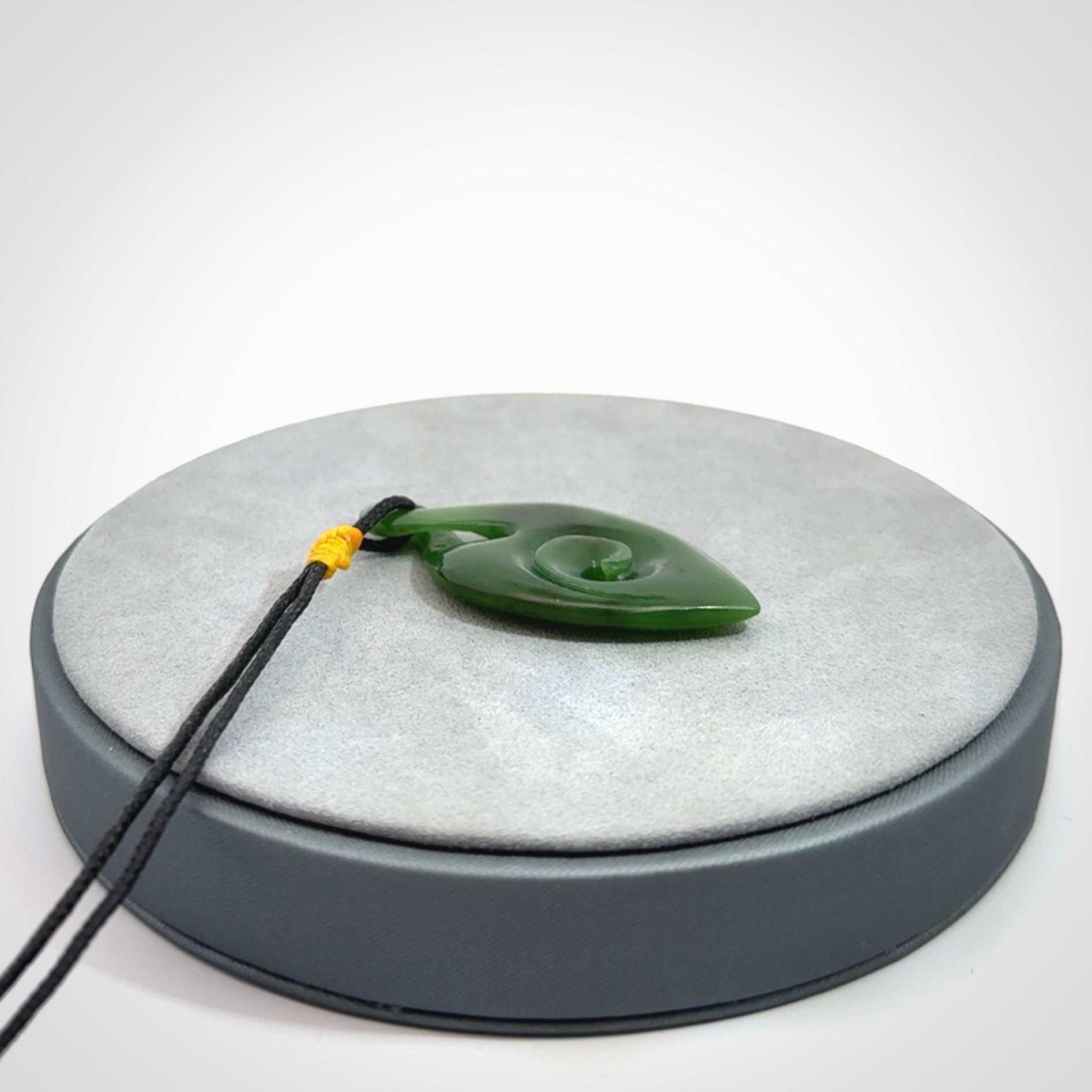 Ross Crump twist with koru pendant. Hand carved from rare New Zealand jade this is a beautiful pounamu pendant. The cord is a black colour and is length adjustable. It has a little spiral floret popper at the top of the pendant. It is a delicate and very beautiful greenstone pendant. For sale online by NZ Pacific.
