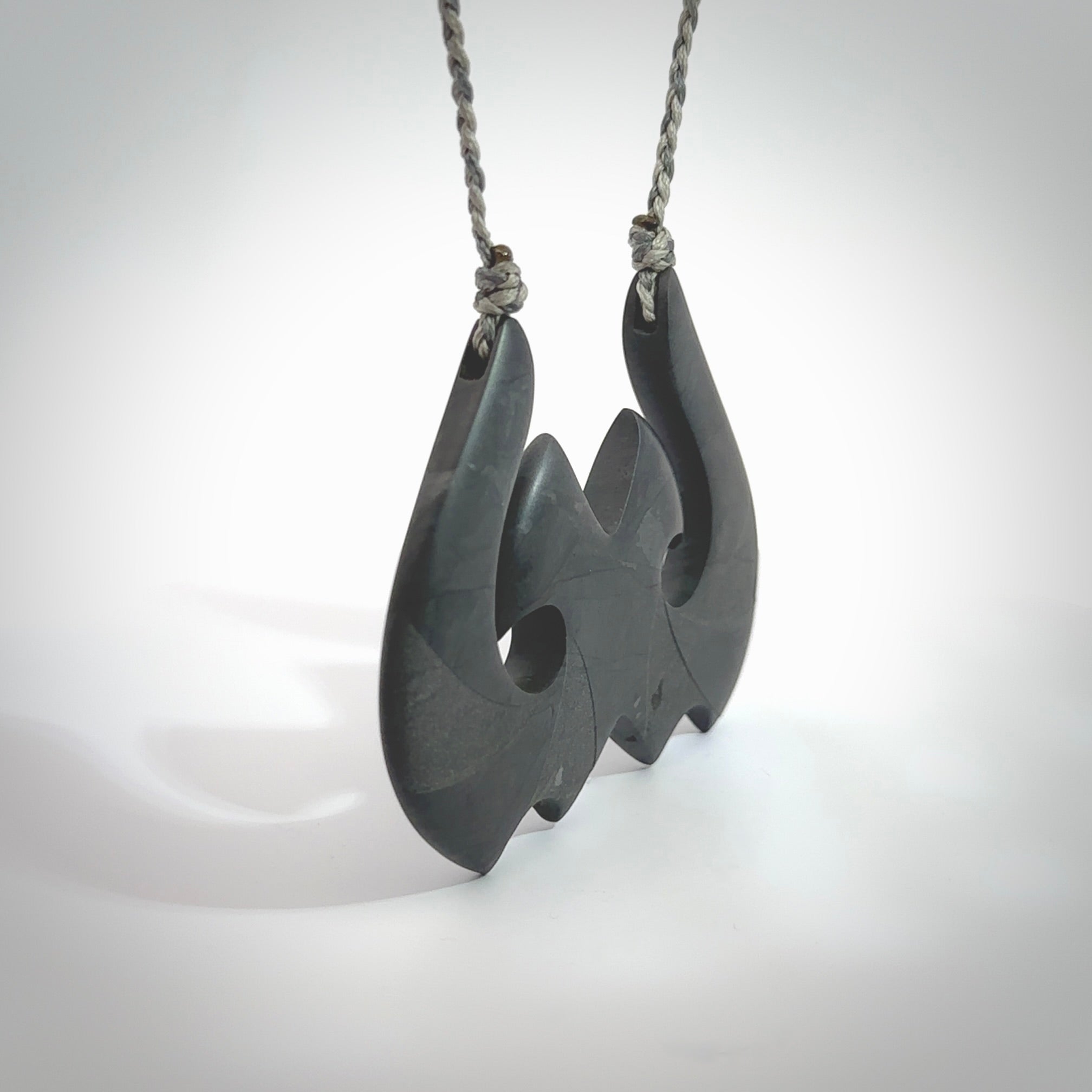A hand carved large New Zealand Argillite double Hook, Matau, necklace. The cord is a black colour and is adjustable in length. A large sized hand made double hook necklace by New Zealand artist Rueben Tipene. One off work of art to wear.