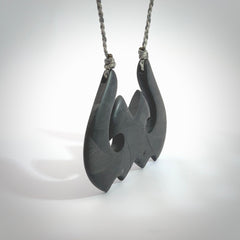 A hand carved large New Zealand Argillite double Hook, Matau, necklace. The cord is a black colour and is adjustable in length. A large sized hand made double hook necklace by New Zealand artist Rueben Tipene. One off work of art to wear.
