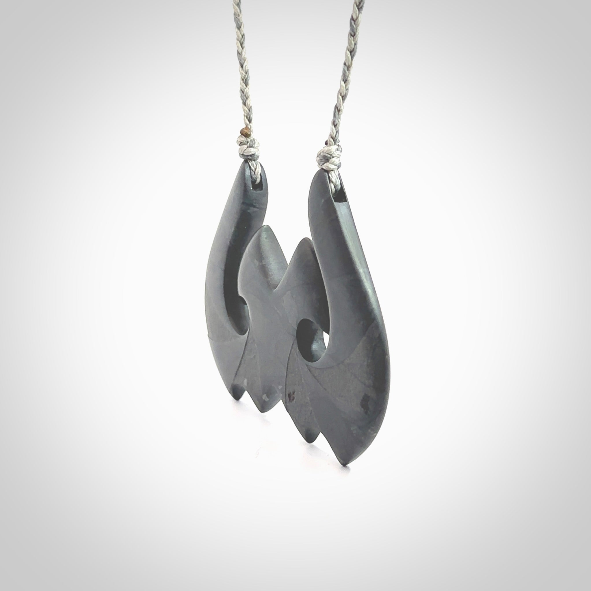 A hand carved large New Zealand Argillite double Hook, Matau, necklace. The cord is a black colour and is adjustable in length. A large sized hand made double hook necklace by New Zealand artist Rueben Tipene. One off work of art to wear.