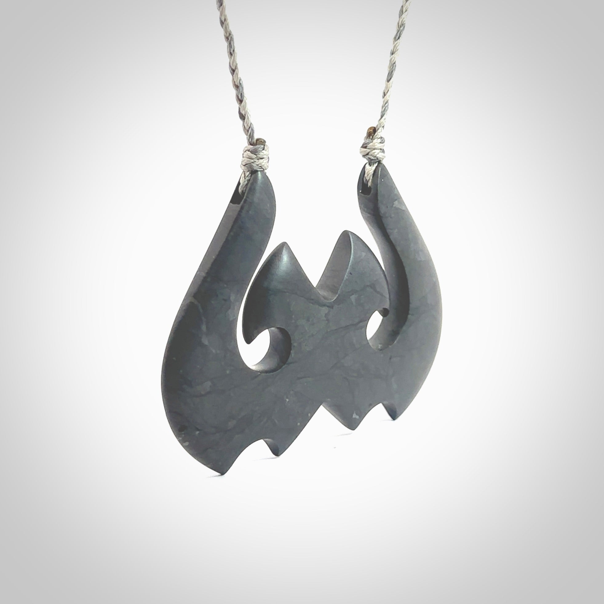 A hand carved large New Zealand Argillite double Hook, Matau, necklace. The cord is a black colour and is adjustable in length. A large sized hand made double hook necklace by New Zealand artist Rueben Tipene. One off work of art to wear.