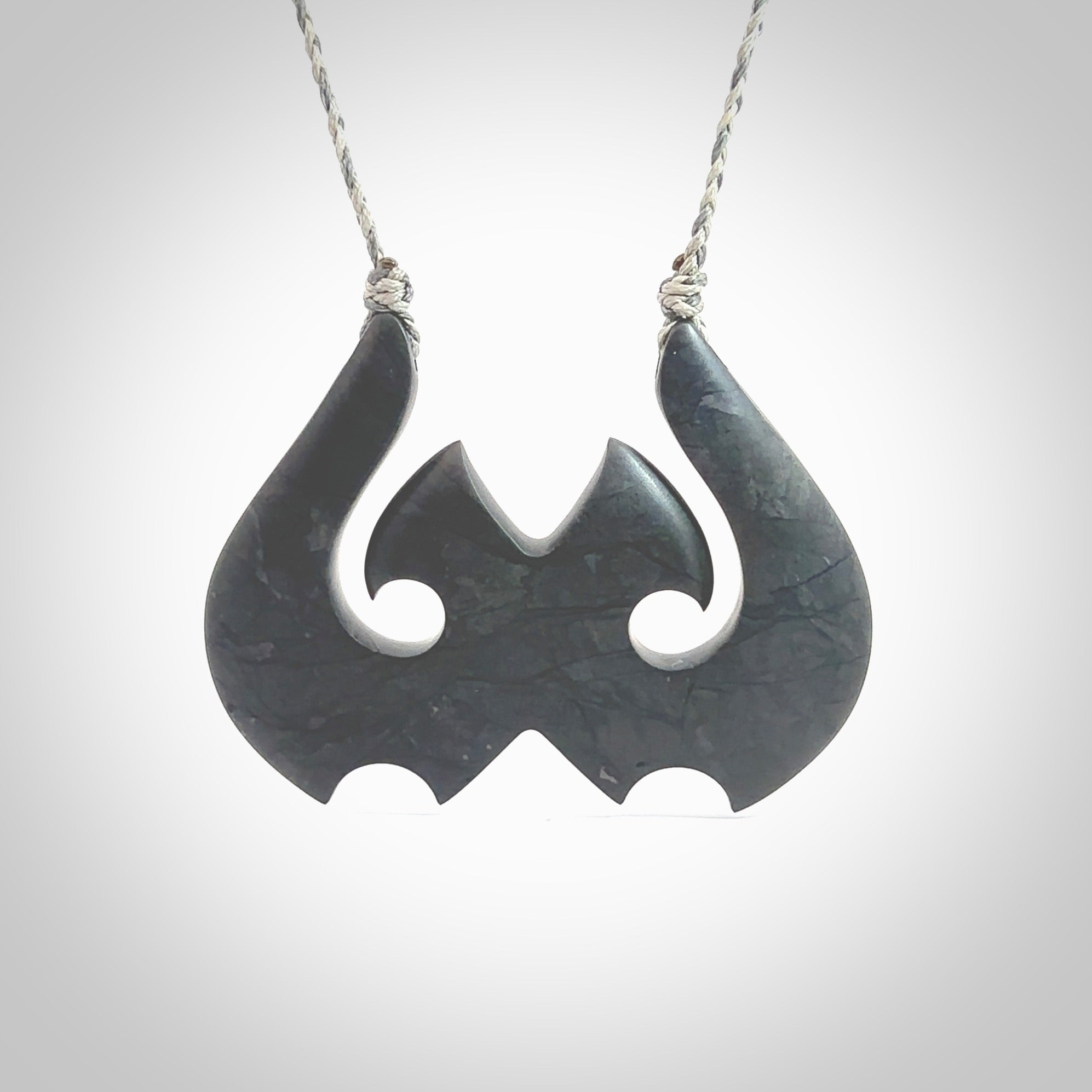 A hand carved large New Zealand Argillite double Hook, Matau, necklace. The cord is a black colour and is adjustable in length. A large sized hand made double hook necklace by New Zealand artist Rueben Tipene. One off work of art to wear.