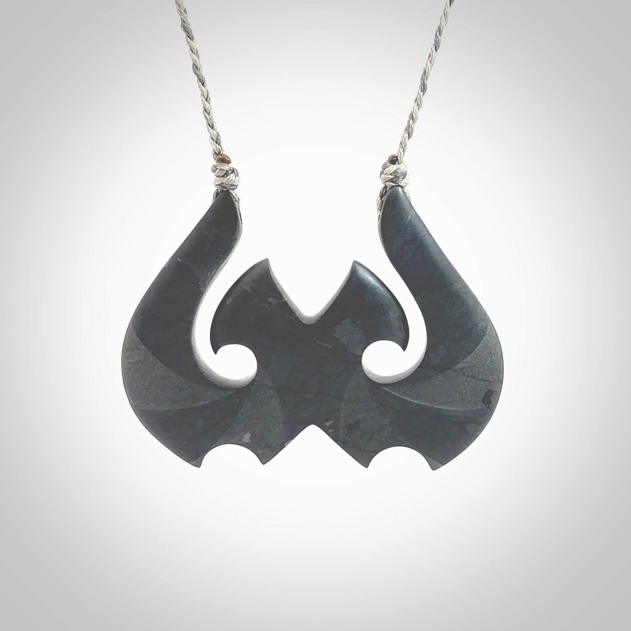 A hand carved large New Zealand Argillite double Hook, Matau, necklace. The cord is a black colour and is adjustable in length. A large sized hand made double hook necklace by New Zealand artist Rueben Tipene. One off work of art to wear.