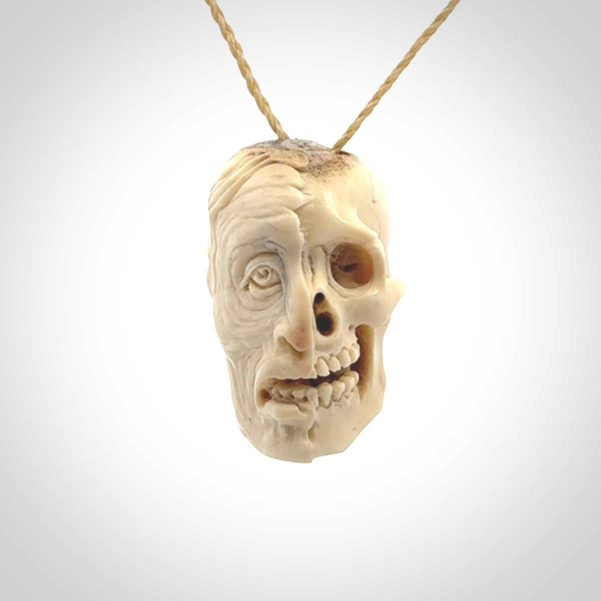 This photo shows a mummy skull pendant hand carved in deer antler. It is provided with a plaited cord necklace which is length adjustable.
