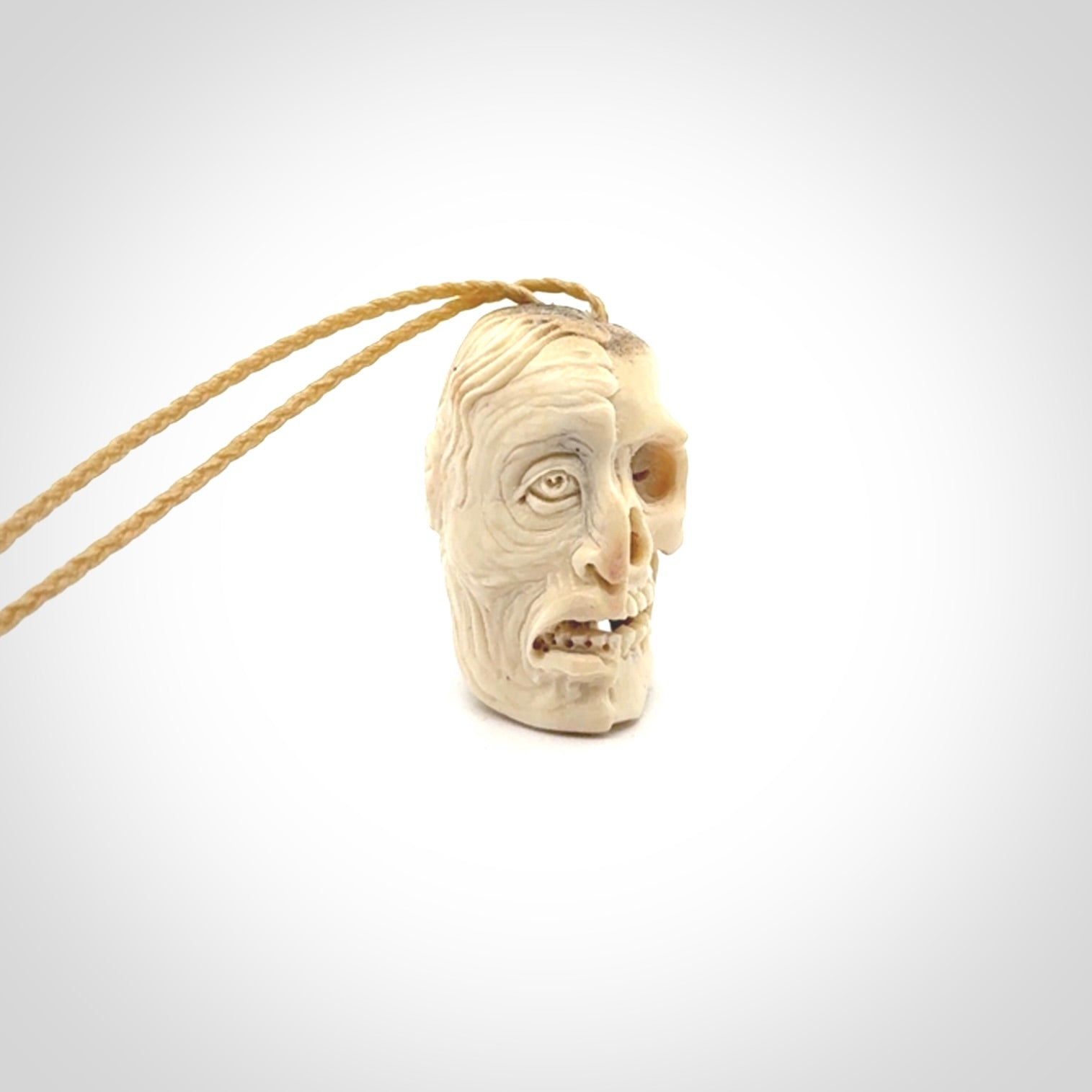 This photo shows a mummy skull pendant hand carved in deer antler. It is provided with a plaited cord necklace which is length adjustable.