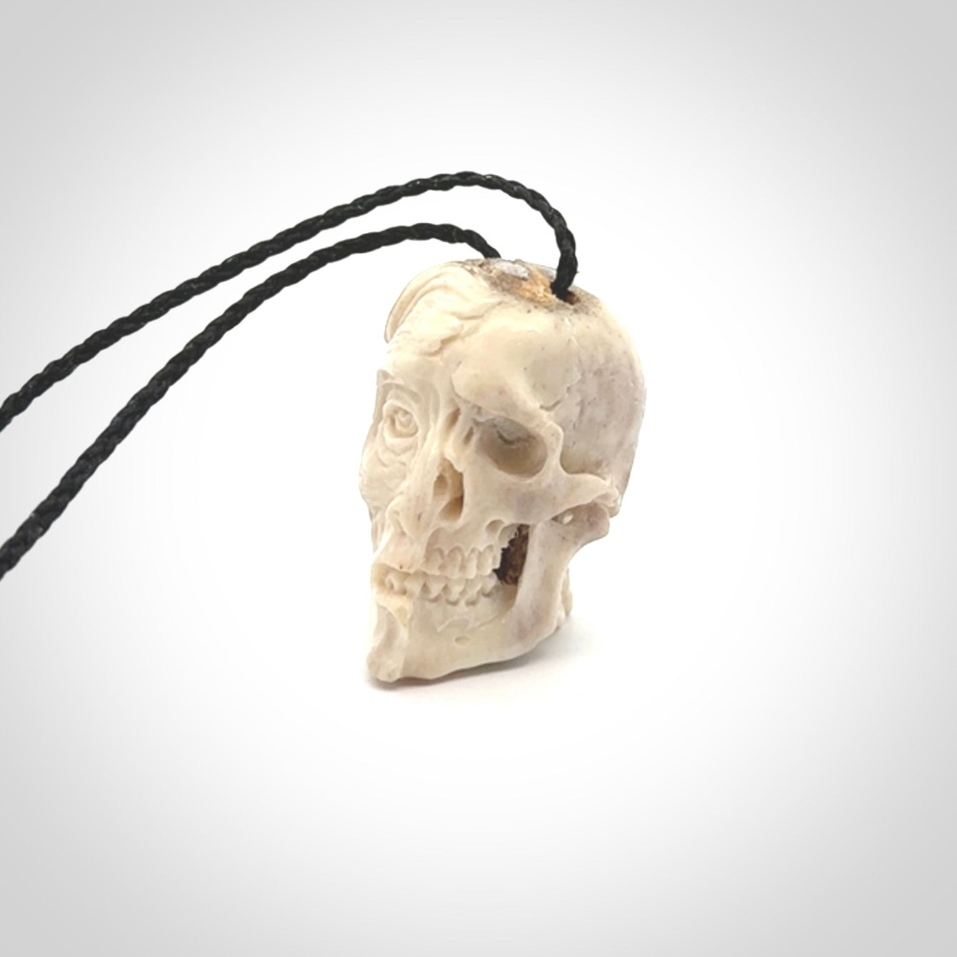 This photo shows a mummy skull pendant hand carved in deer antler. It is provided with a plaited cord necklace which is length adjustable.