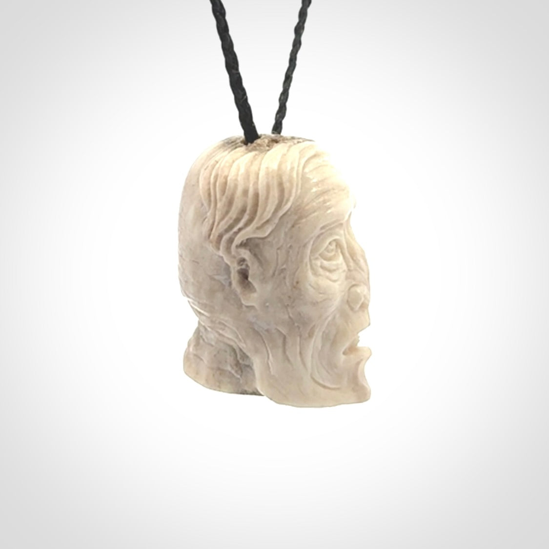 This photo shows a mummy skull pendant hand carved in deer antler. It is provided with a plaited cord necklace which is length adjustable.