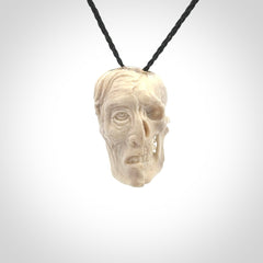This photo shows a mummy skull pendant hand carved in deer antler. It is provided with a plaited cord necklace which is length adjustable.