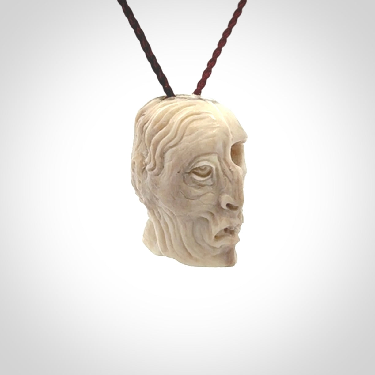 This photo shows a mummy skull pendant hand carved in deer antler. It is provided with a plaited cord necklace which is length adjustable.