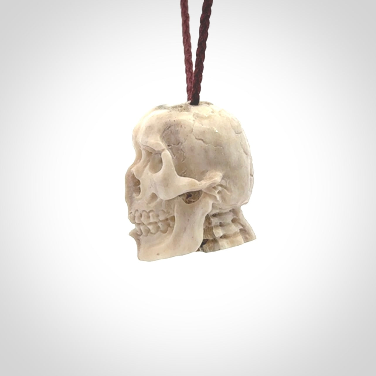 This photo shows a mummy skull pendant hand carved in deer antler. It is provided with a plaited cord necklace which is length adjustable.