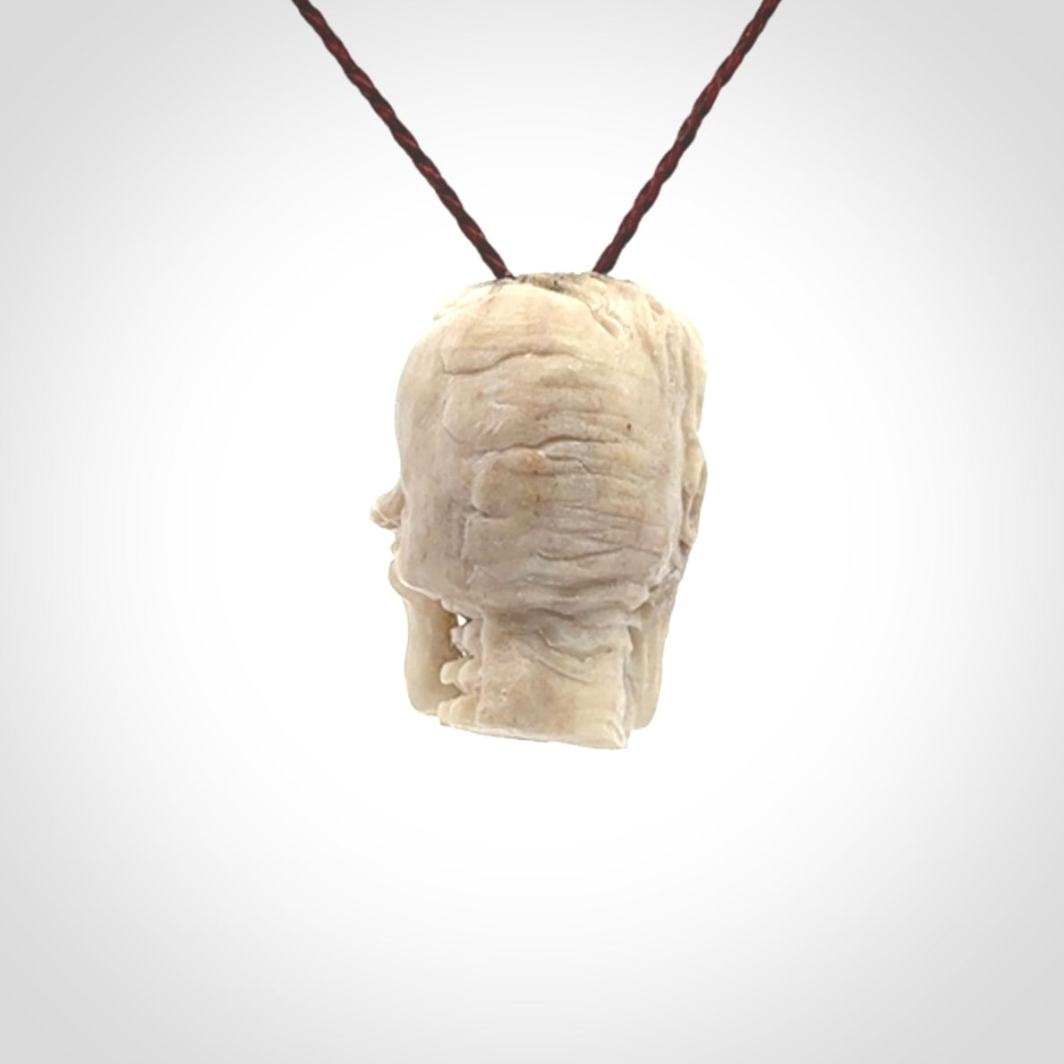 This photo shows a mummy skull pendant hand carved in deer antler. It is provided with a plaited cord necklace which is length adjustable.