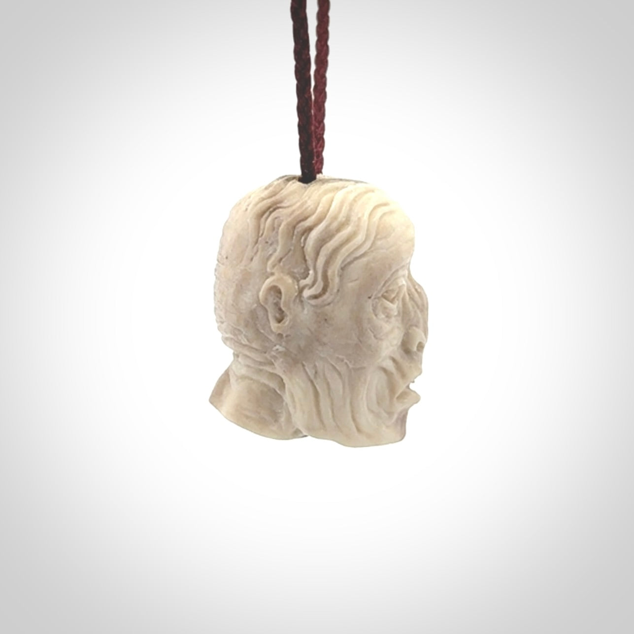 This photo shows a mummy skull pendant hand carved in deer antler. It is provided with a plaited cord necklace which is length adjustable.