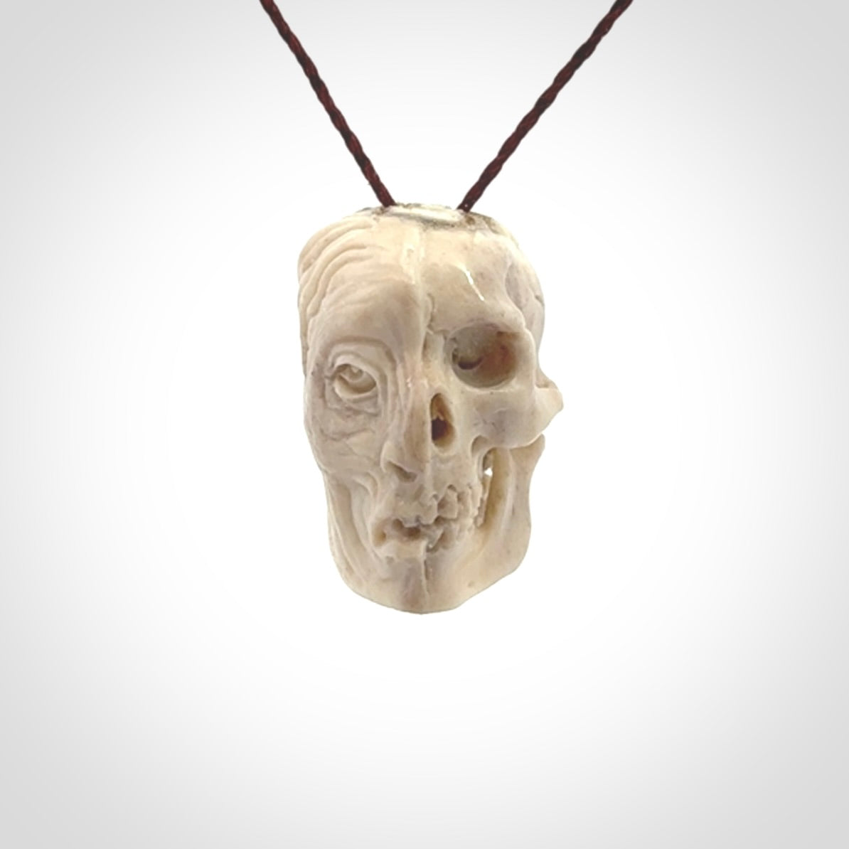 This photo shows a mummy skull pendant hand carved in deer antler. It is provided with a plaited cord necklace which is length adjustable.