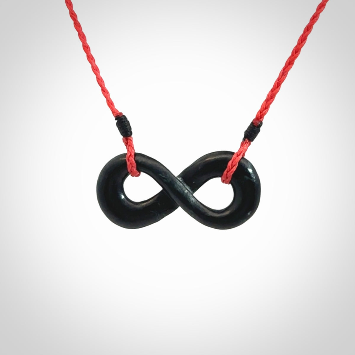This piece is a fine, delicate eternity shaped pendant. It was carved from a lovely dark piece of black jade. It is suspended on an red plaited cord that is length adjustable.