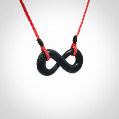 This piece is a fine, delicate eternity shaped pendant. It was carved from a lovely dark piece of black jade. It is suspended on an red plaited cord that is length adjustable.