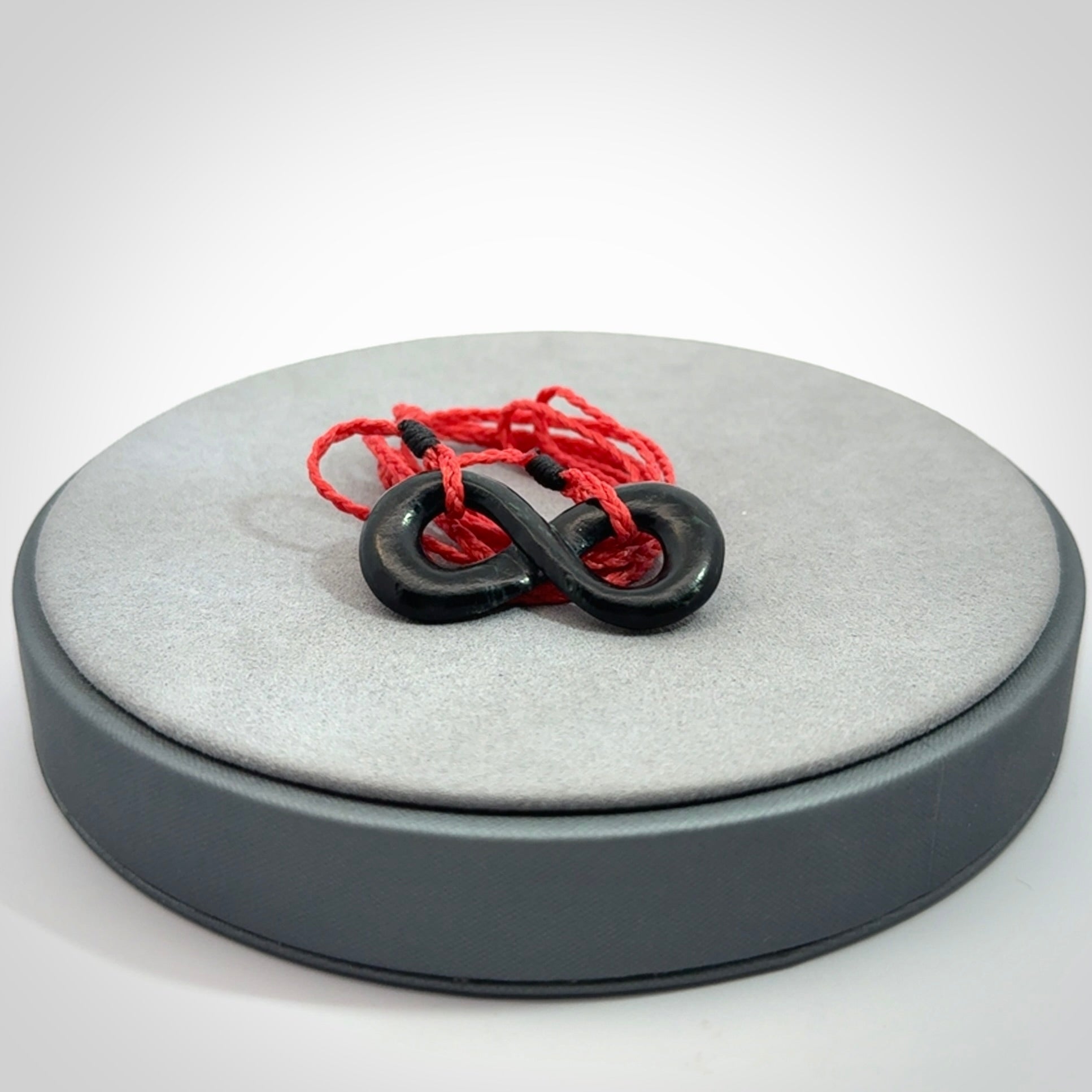 This piece is a fine, delicate eternity shaped pendant. It was carved from a lovely dark piece of black jade. It is suspended on an red plaited cord that is length adjustable.