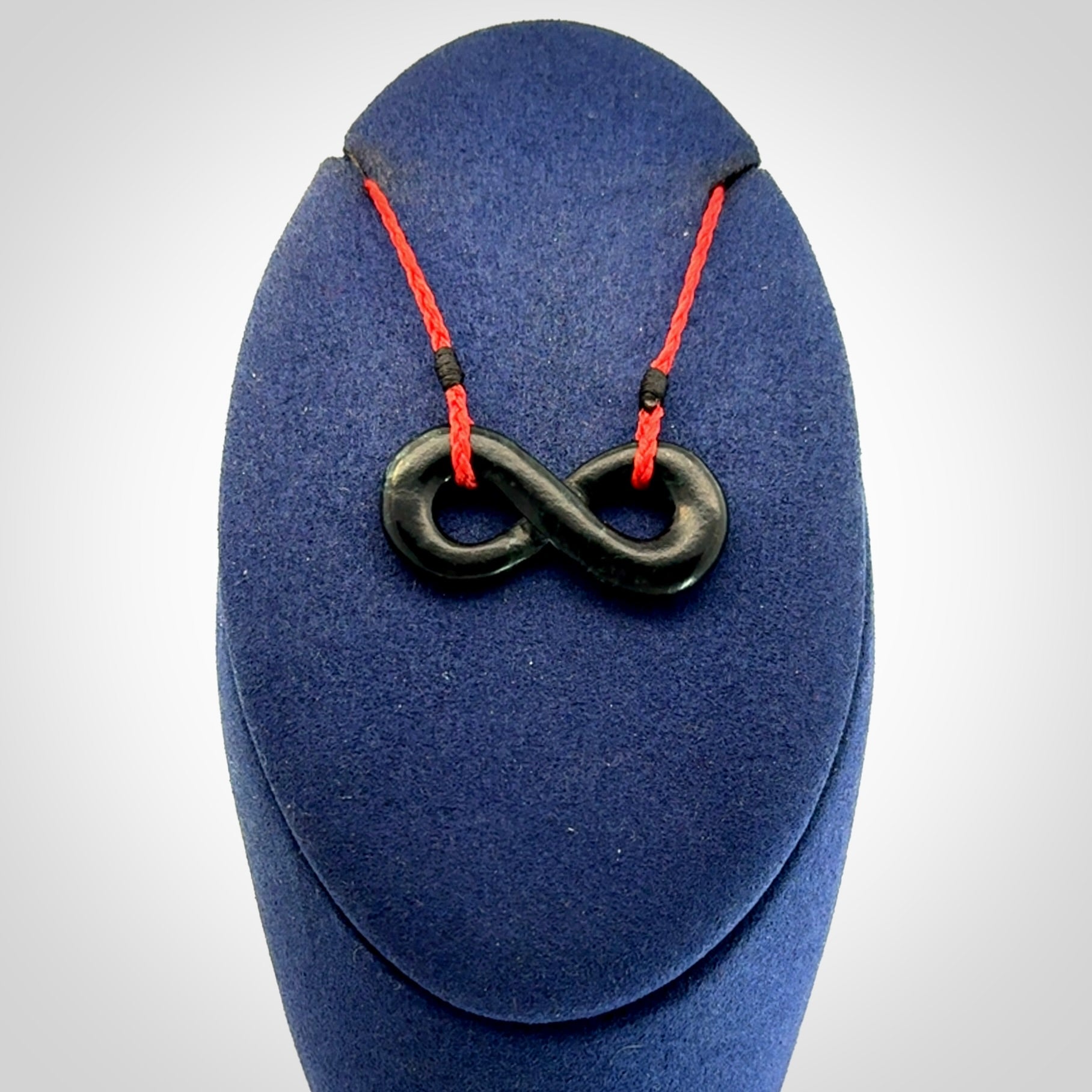This piece is a fine, delicate eternity shaped pendant. It was carved from a lovely dark piece of black jade. It is suspended on an red plaited cord that is length adjustable.