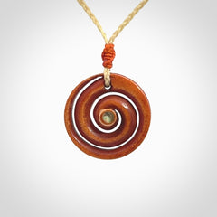 A hand carved and intricate koru pendant made for us by Yuri Terenyi. It is suspended from a oat cord with a orange floret and the necklace is adjustable.