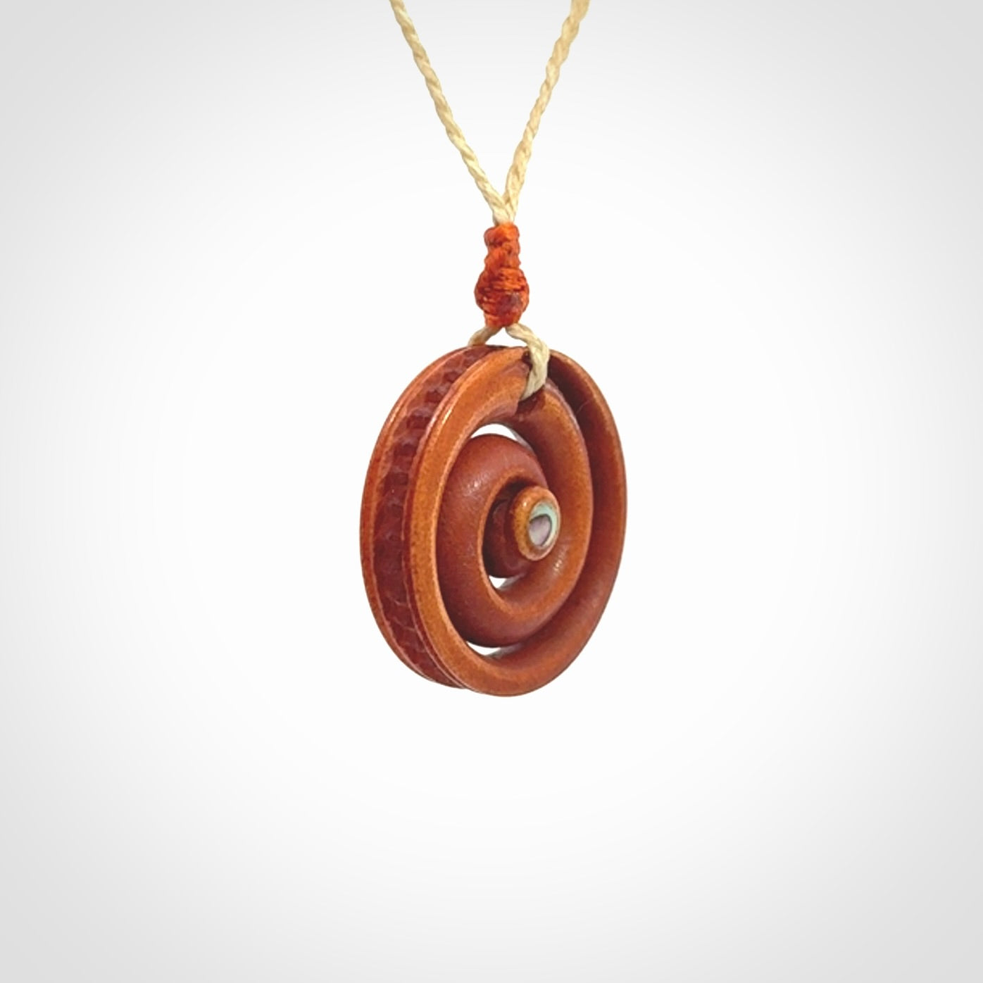 A hand carved and intricate koru pendant made for us by Yuri Terenyi. It is suspended from a oat cord with a orange floret and the necklace is adjustable.