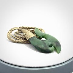 This is a beautiful jade hook with a little decorative koru carved into the bottom. It is a chunky piece but beautifully balanced so doesn't look heavy. The cord and the binding on the top is a khaki colour.