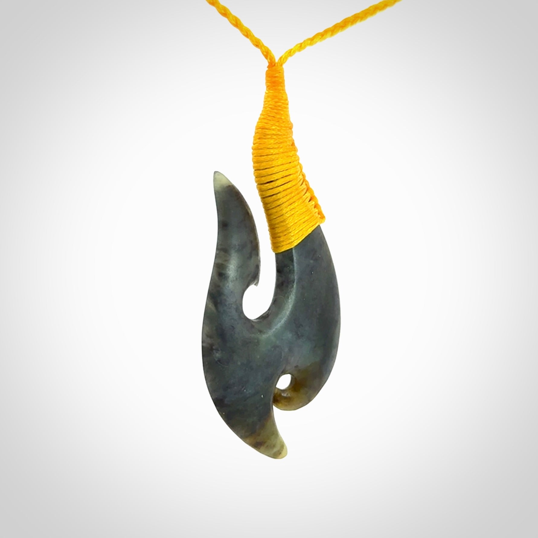This is a beautiful jade hook with a little decorative koru carved into the bottom. It is a chunky piece but beautifully balanced so doesn't look heavy. The cord and the binding on the top is a yellow colour.
