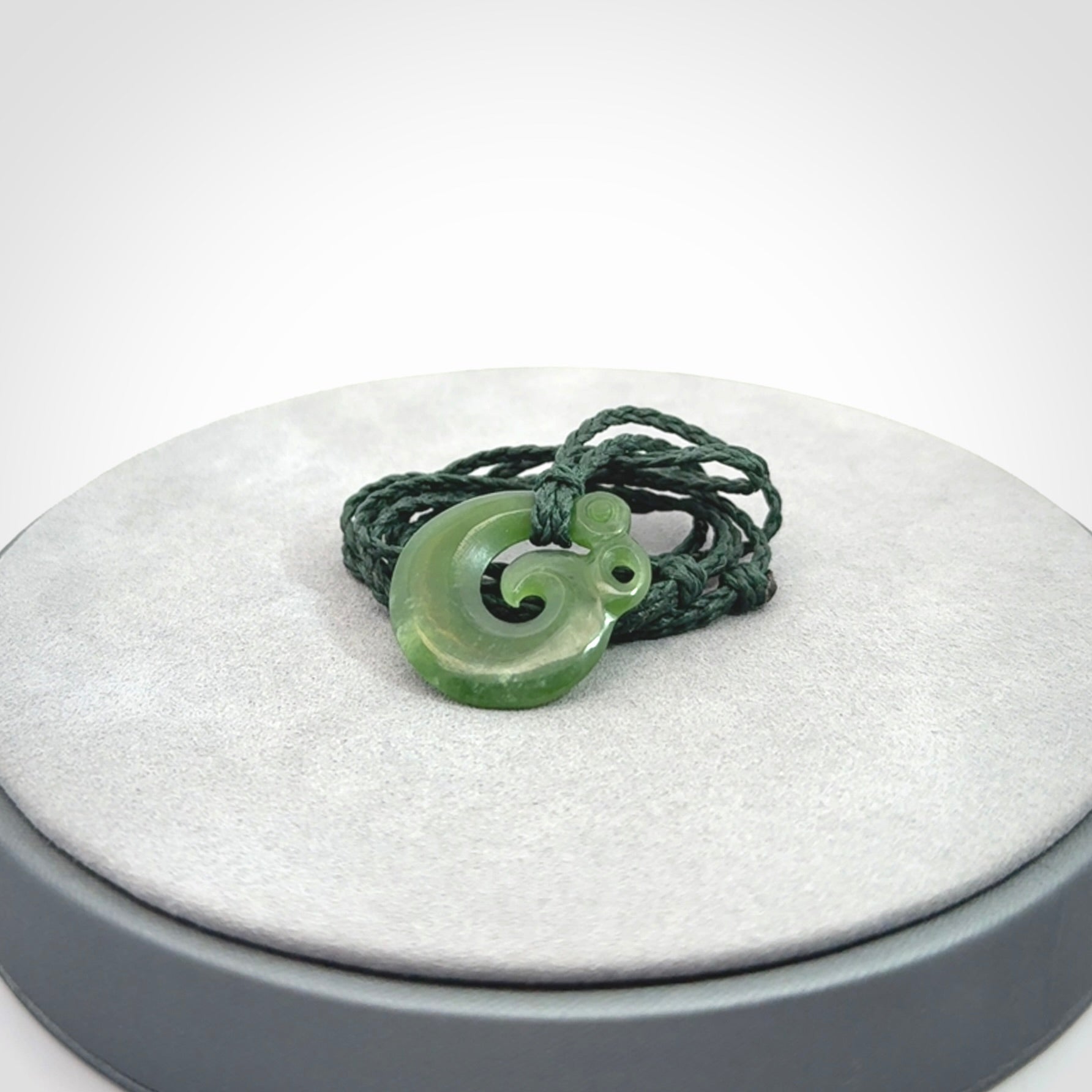 New Zealand Koru Manaia. Hand carved small jade koropepe pendant. Made in New Zealand. Real Jade, pounamu. Provided with an adjustable Manuka Green cord and packaged in a woven kete pouch.