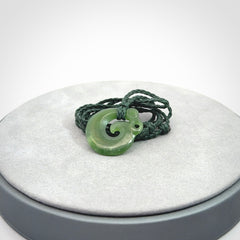 New Zealand Koru Manaia. Hand carved small jade koropepe pendant. Made in New Zealand. Real Jade, pounamu. Provided with an adjustable Manuka Green cord and packaged in a woven kete pouch.