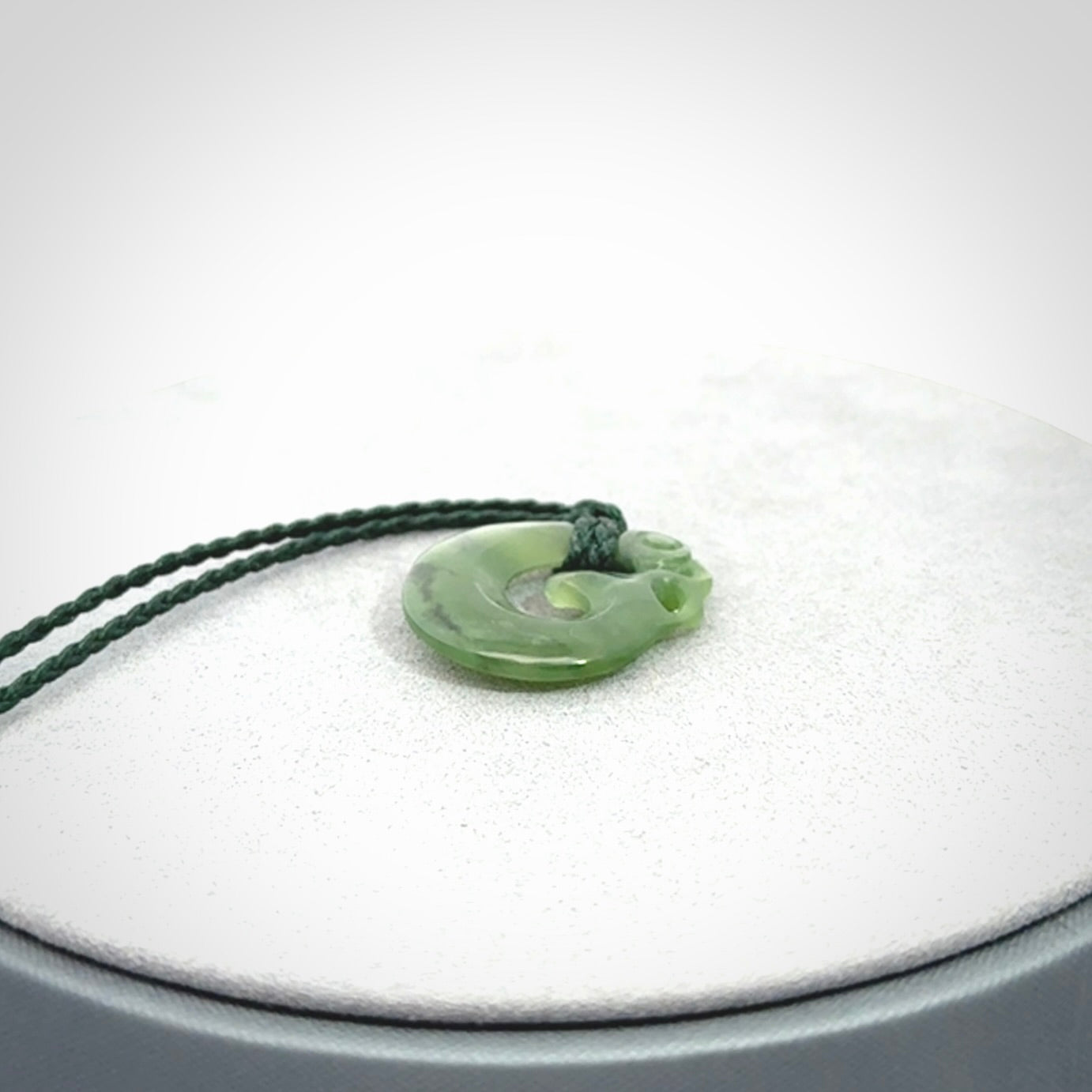 New Zealand Koru Manaia. Hand carved small jade koropepe pendant. Made in New Zealand. Real Jade, pounamu. Provided with an adjustable Manuka Green cord and packaged in a woven kete pouch.
