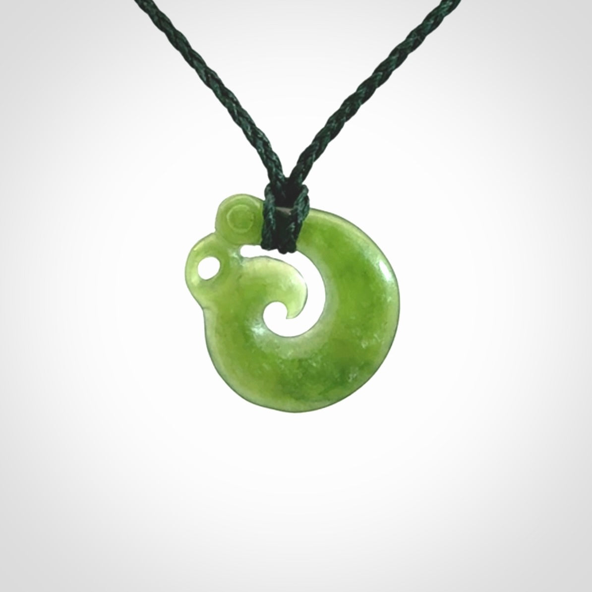 New Zealand Koru Manaia. Hand carved small jade koropepe pendant. Made in New Zealand. Real Jade, pounamu. Provided with an adjustable Manuka Green cord and packaged in a woven kete pouch.