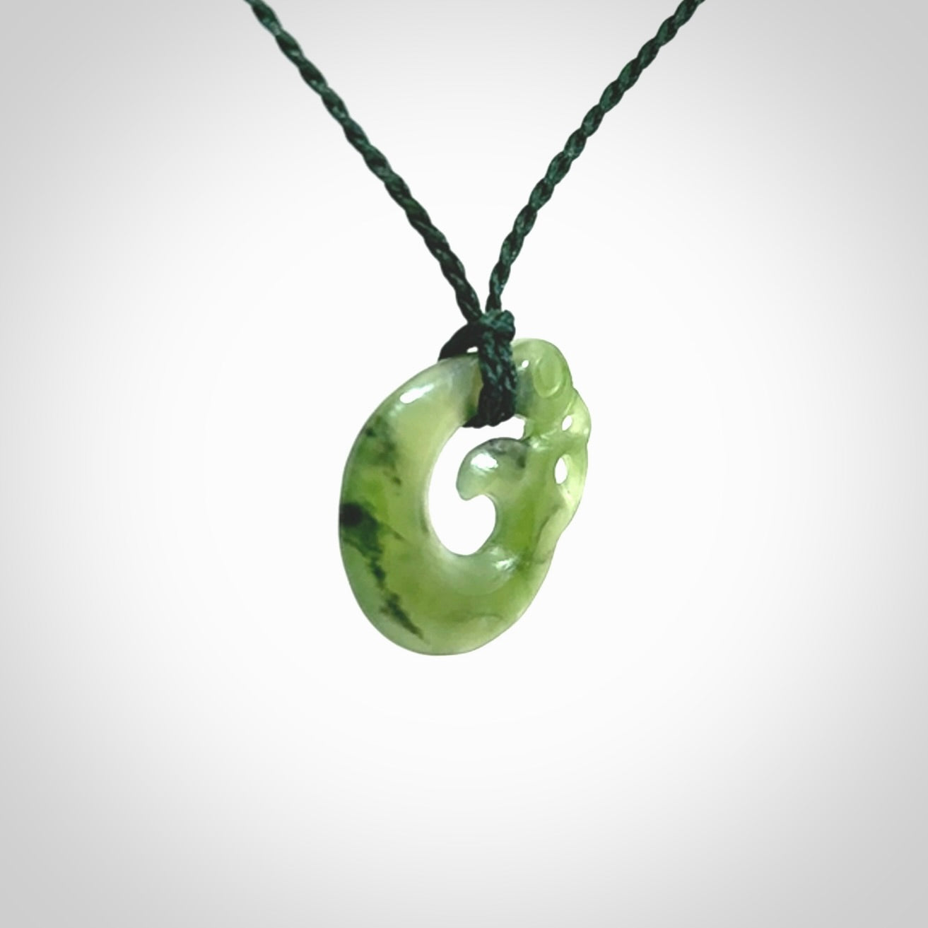 New Zealand Koru Manaia. Hand carved small jade koropepe pendant. Made in New Zealand. Real Jade, pounamu. Provided with an adjustable Manuka Green cord and packaged in a woven kete pouch.