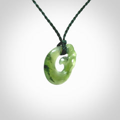 New Zealand Koru Manaia. Hand carved small jade koropepe pendant. Made in New Zealand. Real Jade, pounamu. Provided with an adjustable Manuka Green cord and packaged in a woven kete pouch.