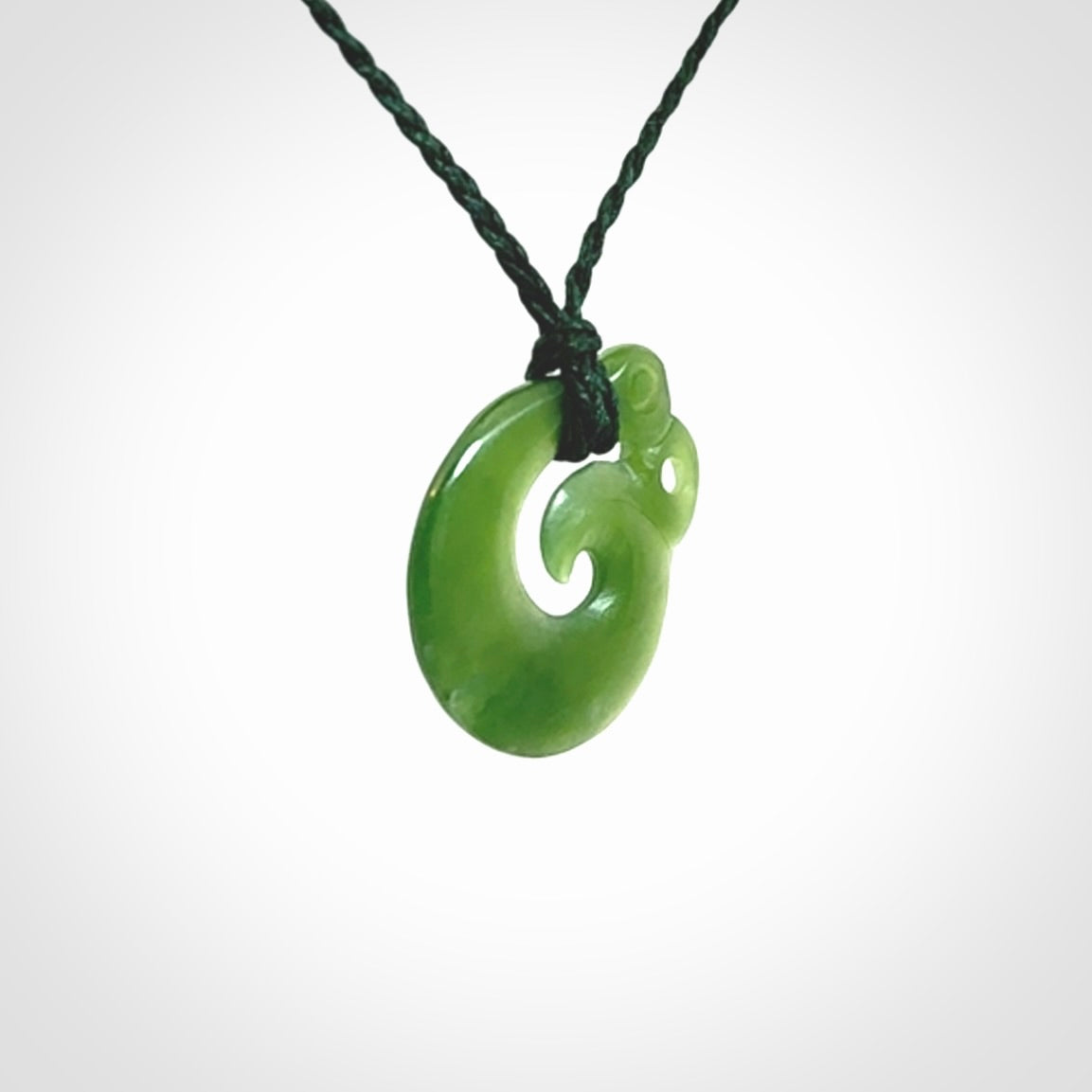 New Zealand Koru Manaia. Hand carved small jade koropepe pendant. Made in New Zealand. Real Jade, pounamu. Provided with an adjustable Manuka Green cord and packaged in a woven kete pouch.