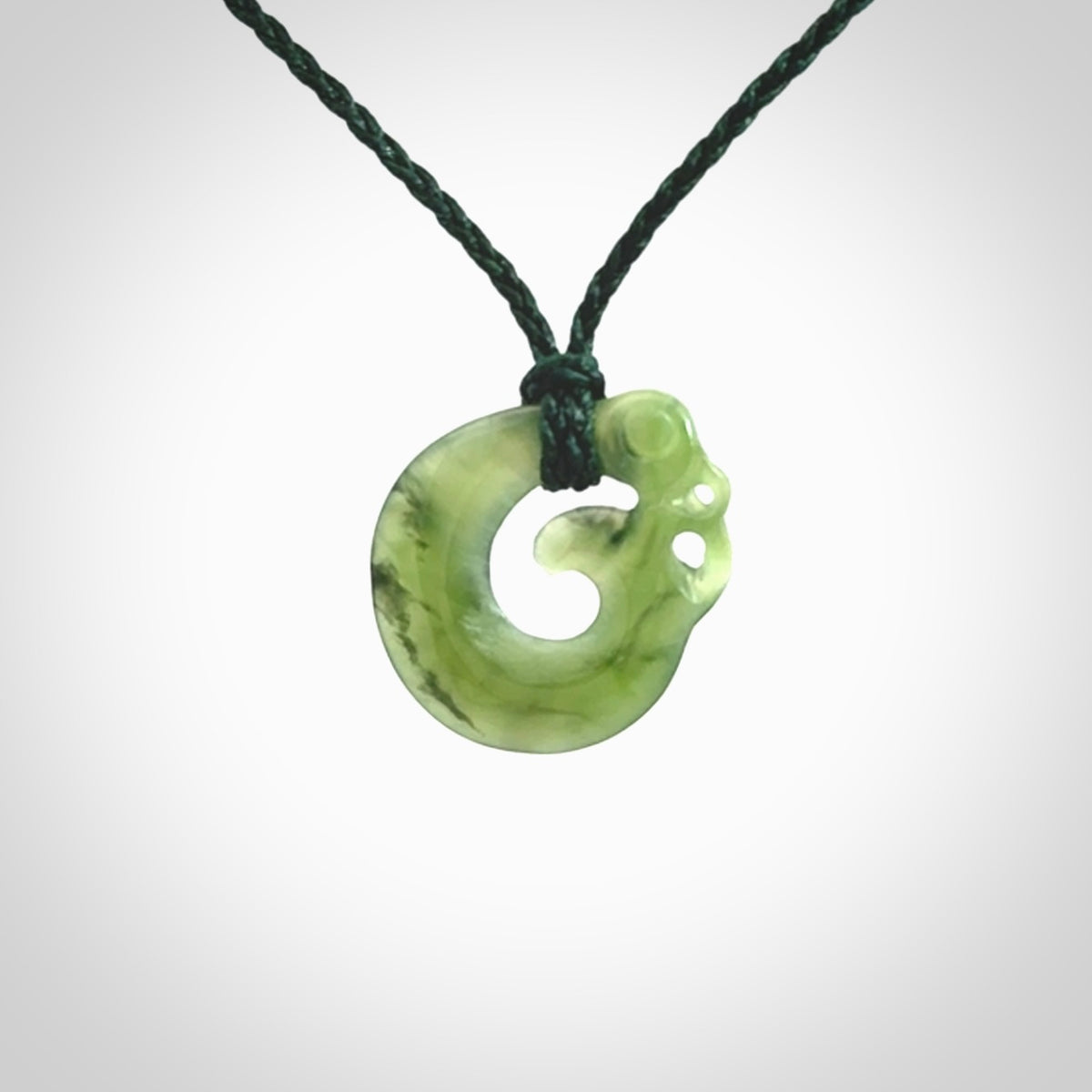 New Zealand Koru Manaia. Hand carved small jade koropepe pendant. Made in New Zealand. Real Jade, pounamu. Provided with an adjustable Manuka Green cord and packaged in a woven kete pouch.