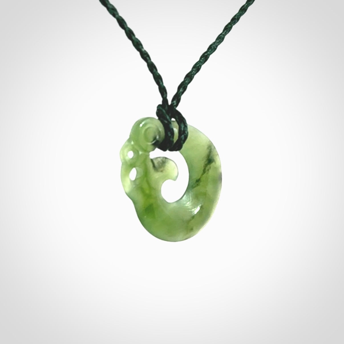New Zealand Koru Manaia. Hand carved small jade koropepe pendant. Made in New Zealand. Real Jade, pounamu. Provided with an adjustable Manuka Green cord and packaged in a woven kete pouch.