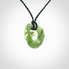 New Zealand Koru Manaia. Hand carved small jade koropepe pendant. Made in New Zealand. Real Jade, pounamu. Provided with an adjustable Manuka Green cord and packaged in a woven kete pouch.