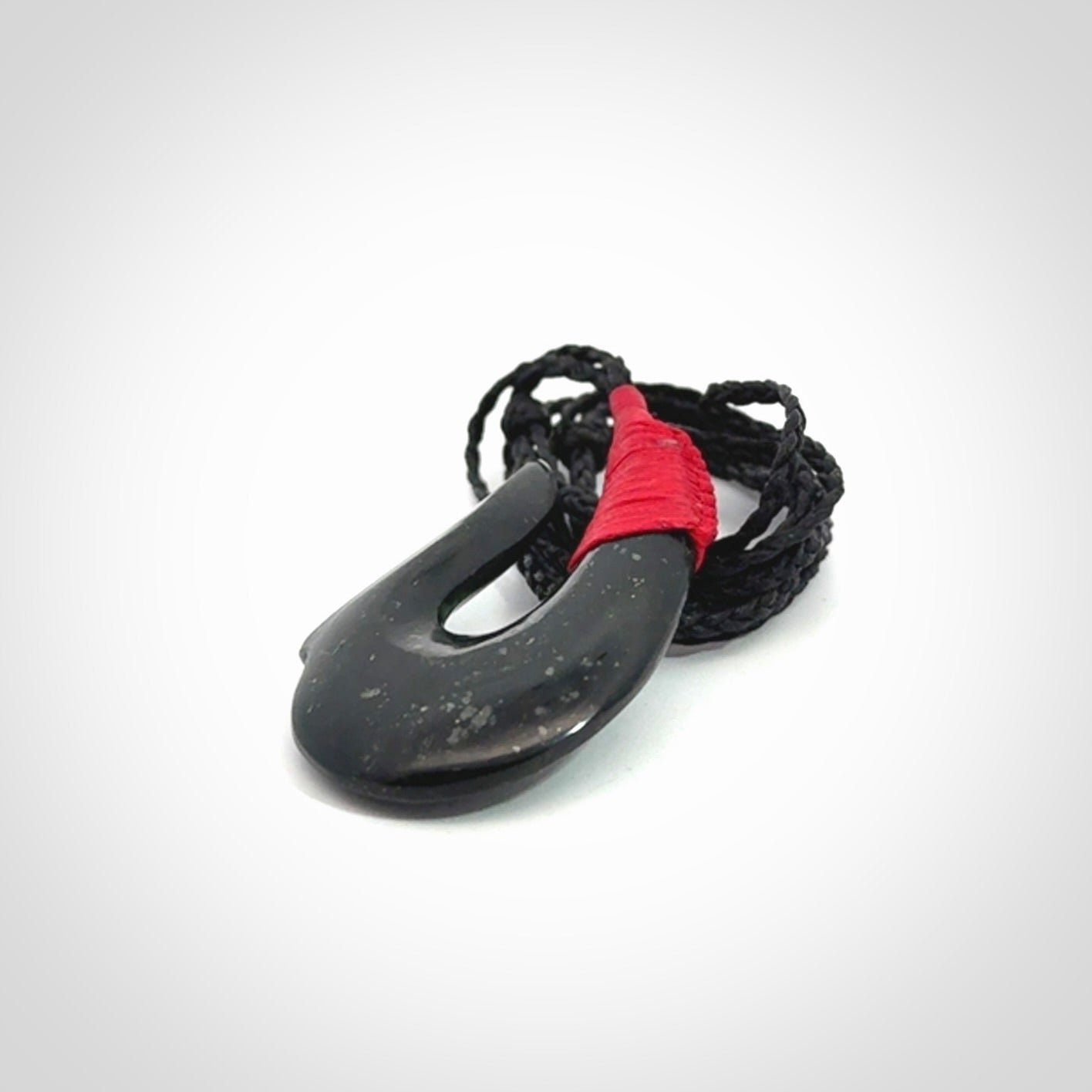 This photo shows a New Zealand Tangiwai hook, or matau, pendant. The plaited cord is black and the length can be adjusted.