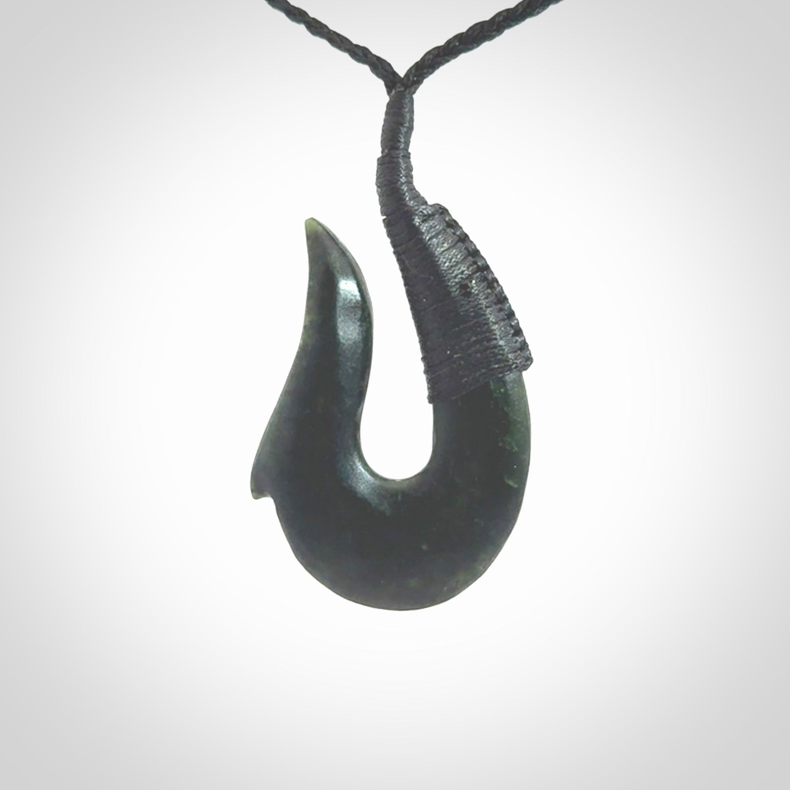 This photo shows a greenstone hook, or matau, pendant. It is a beautiful deep green jade. The cord is plaited black and the length can be adjusted.