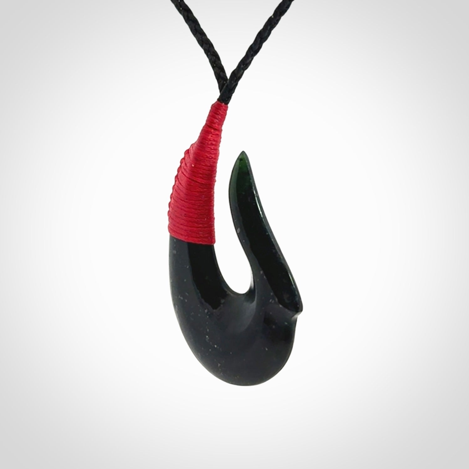 This photo shows a New Zealand Tangiwai hook, or matau, pendant. The plaited cord is black and the length can be adjusted.