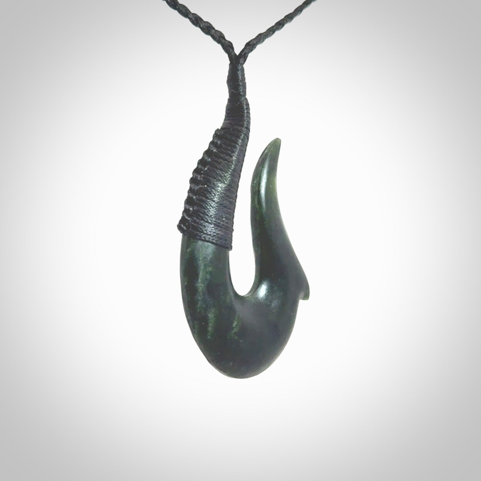 This photo shows a greenstone hook, or matau, pendant. It is a beautiful deep green jade. The cord is plaited black and the length can be adjusted.