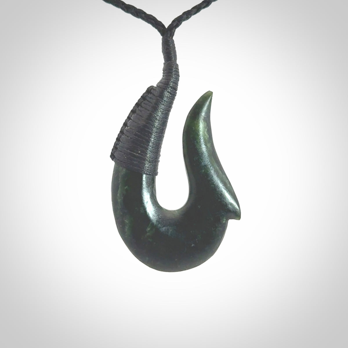 This photo shows a greenstone hook, or matau, pendant. It is a beautiful deep green jade. The cord is plaited black and the length can be adjusted.