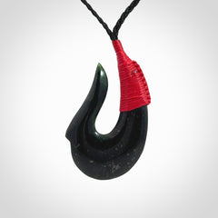 This photo shows a New Zealand Tangiwai hook, or matau, pendant. The plaited cord is black and the length can be adjusted.