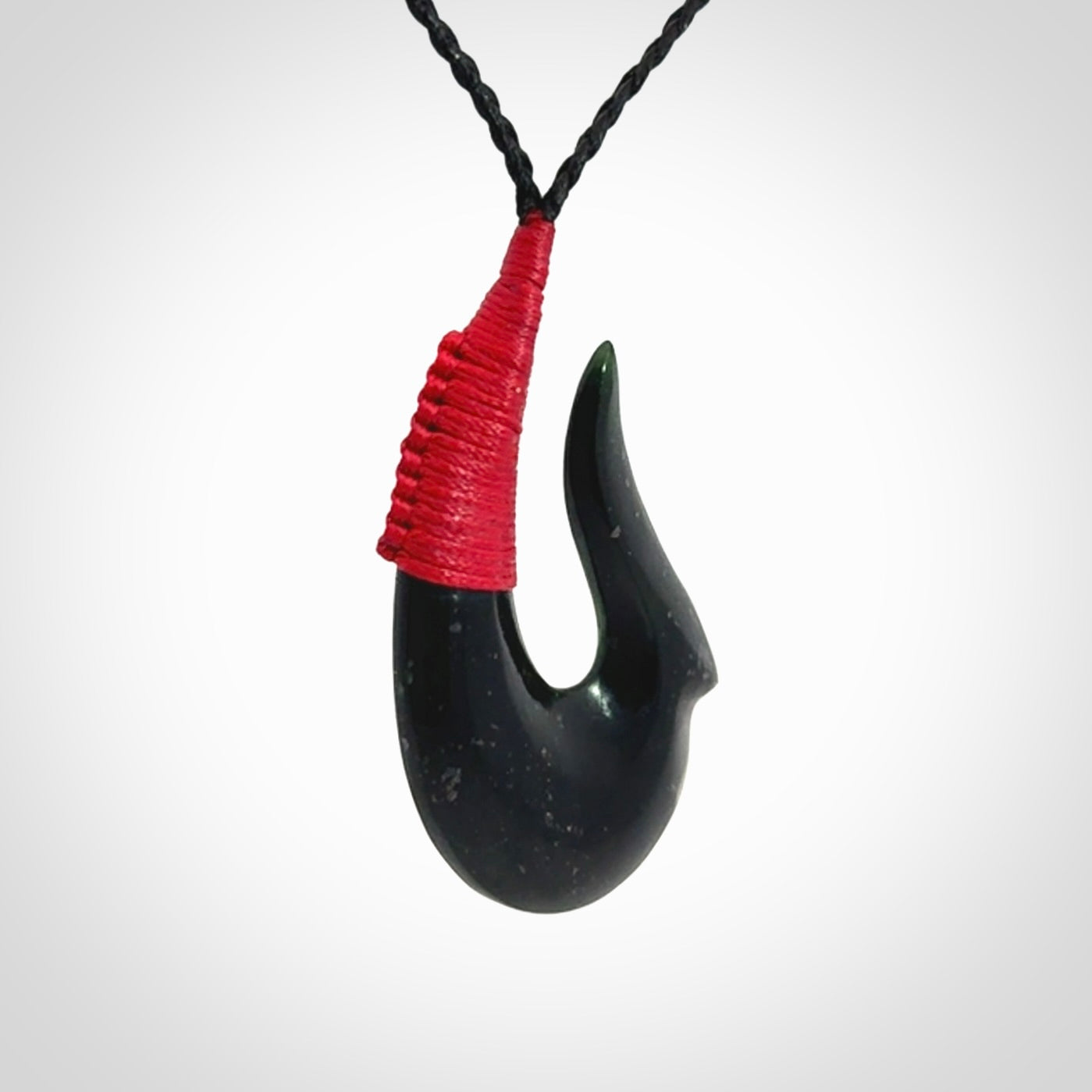 This photo shows a New Zealand Tangiwai hook, or matau, pendant. The plaited cord is black and the length can be adjusted.