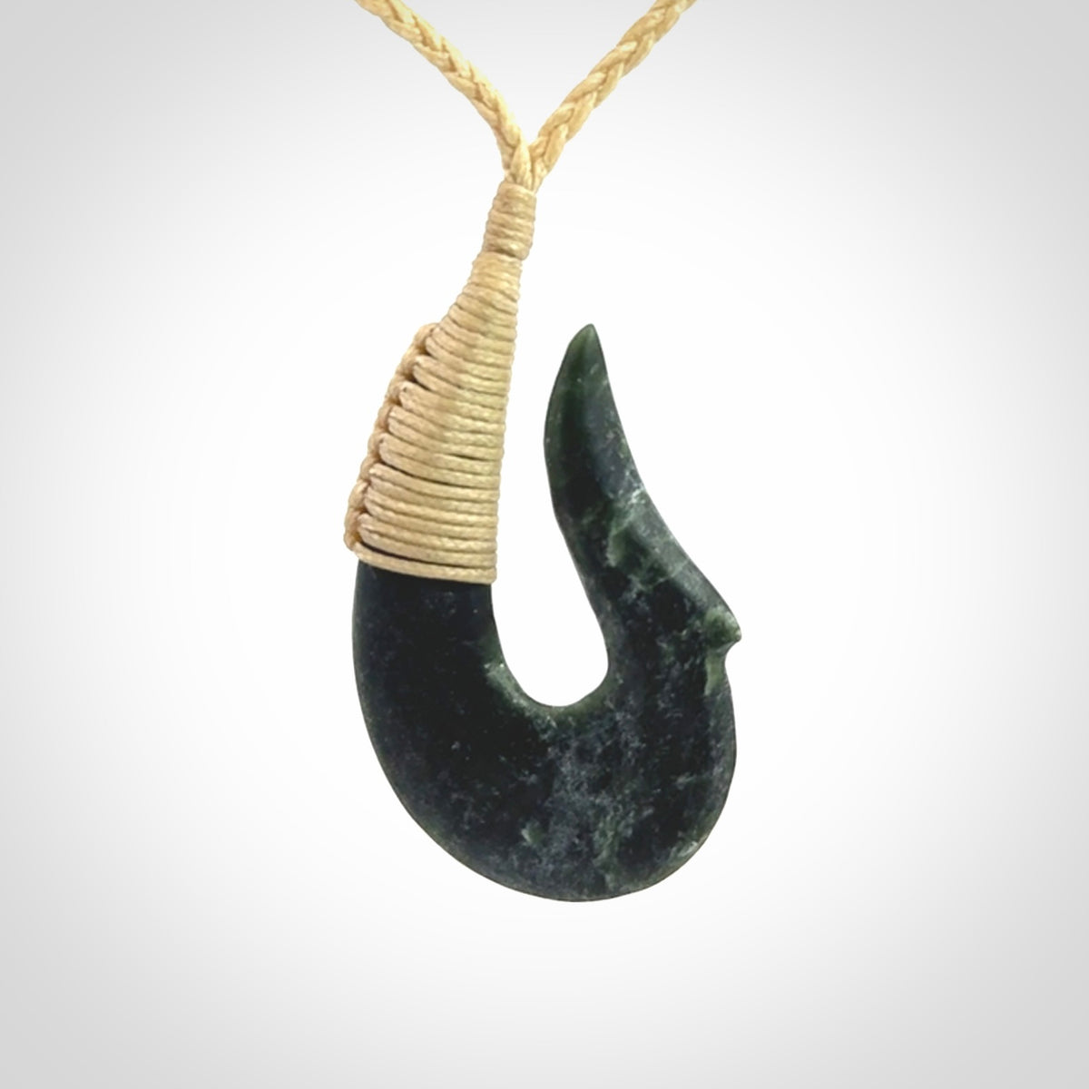 This photo shows a greenstone hook, or matau, pendant. It is a beautiful deep green jade. The cord is plaited and the length can be adjusted.