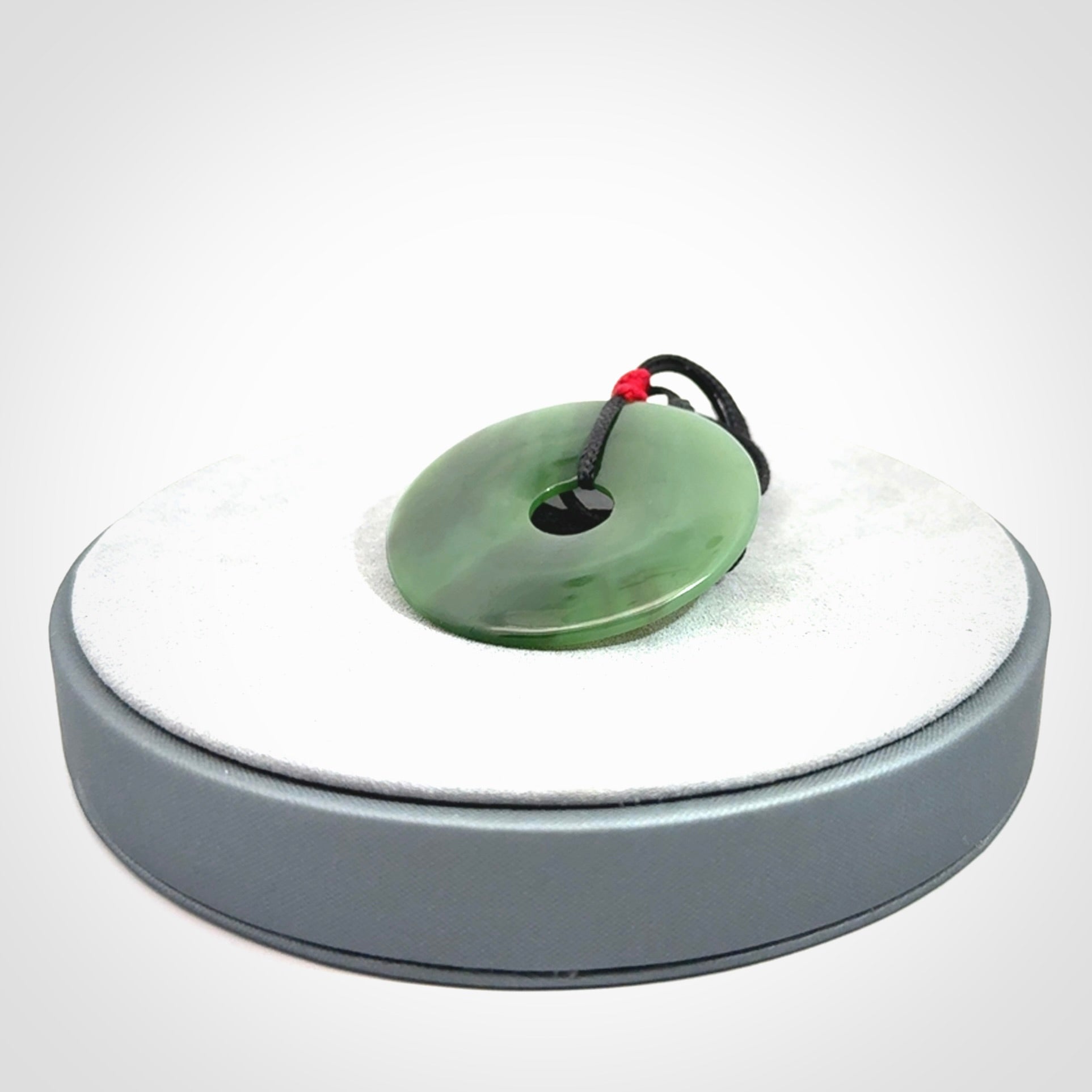 This picture shows a large hand-carved disc pendant. It is carved from British Columbian jade and is suspended from a hand-plaited, black cord. Free delivery worldwide. BC Jade contemporary necklace.